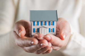 Bild på ett hus i två händer, symboliserar att man tar hand om sitt hus även om man inte kan betala lånet pga. sjukdom t.ex.